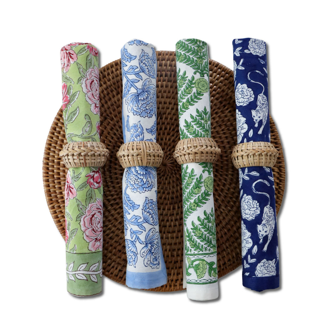 Four rolled block printed napkins in rattan rings on a woven charger