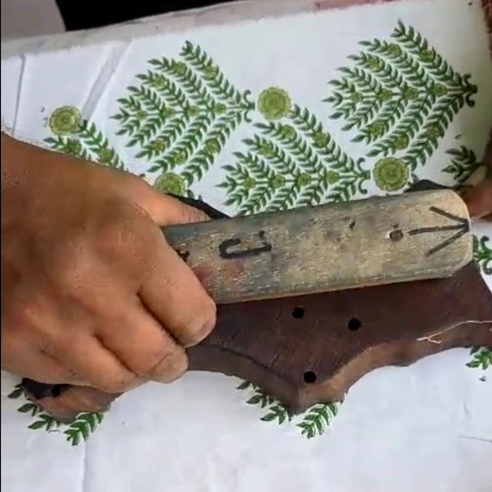 A carved wooden block being pressed by hand onto hand block printed cotton